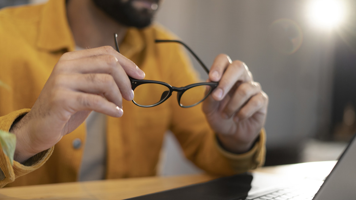 Un homme tient ses lunettes de vue à la main devant son ordinateur portable.